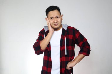 Genç Asyalı kameraya bakıyor ve düşünüyor, kafası karışık bir ifade. Beyaz arkaplanda vücut portresini kapat