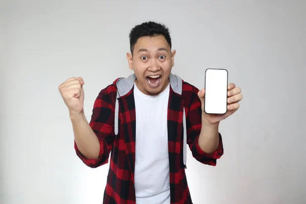 Portrait of young young Asian man presenting smart phone mockup with happy cheerful expression, winning gesture