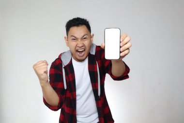 Genç Asyalı adamın portresi akıllı telefon modelini mutlu bir ifadeyle sunuyor, kazanan bir jest.