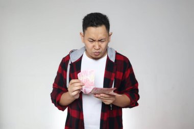 Endonezya rupiasını elinde tutan kafası karışmış Asyalı adam nasıl harcayacağını düşünüyor. Daha fazla para, daha fazla sorun ya da daha az para kavramı