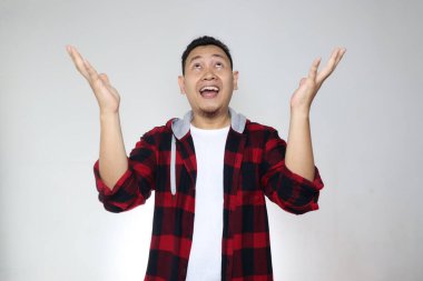 Asyalı adam yukarıdan bir şey alıyor. Mutlu bir gülümseme. Beyaz arka plan üzerinde heyecanlı bir zafer ifadesi.