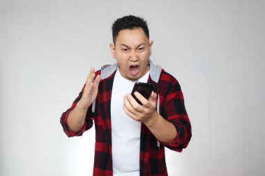 Çekici Asyalı genç adam telefonuyla konuşuyor, kötü haberler alıyor, beyaz arka planda çılgın kızgın bir jest yapıyor.