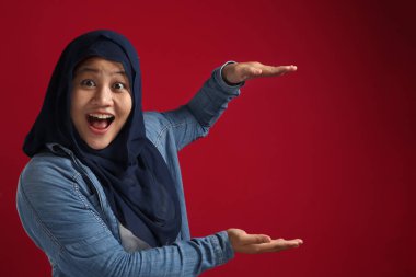 Asyalı genç mutlu Müslüman kadın portresi; elleri arasında bir şey sunuyor; kırmızı arkaplan karşı fotokopi alanı ile