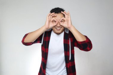 Dürbün yapan mutlu Asyalı genç adam kameraya bakıp gülümsüyor ve gri arka planda stüdyo çekimi yapıyor.