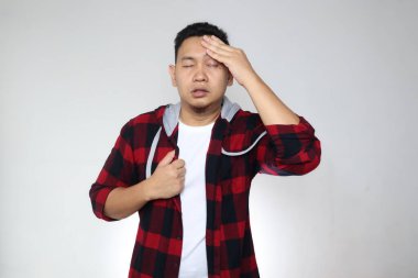 Genç Asyalı adam üşür ve ateşlenir, sersemler ve ürperirler, gri arka plana karşı.