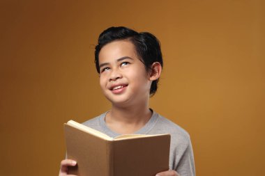 Asyalı mutlu öğrencinin portresi sarı arka planda kitap okurken düşünme ifadesine bakıyor.
