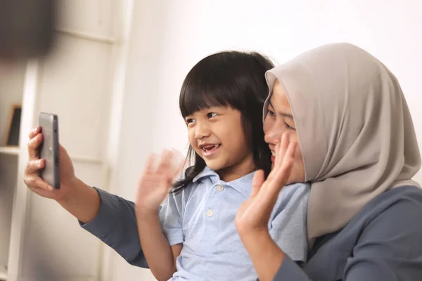 Happy Asian muslim mother and daughter making video call on her phone, distant family gathering via online telecomuting app concept