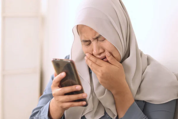 Sad, emotional Asian muslim woman crying and sends a message on mobile phone, bad news on phone concept