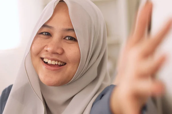 幸せな陽気な美しいアジアのイスラム教徒の女性を身に着けているヒジャーブカメラに手を振って話をし ビデオ通話ジェスチャーを行い 彼女のリビングルームでリラックス — ストック写真