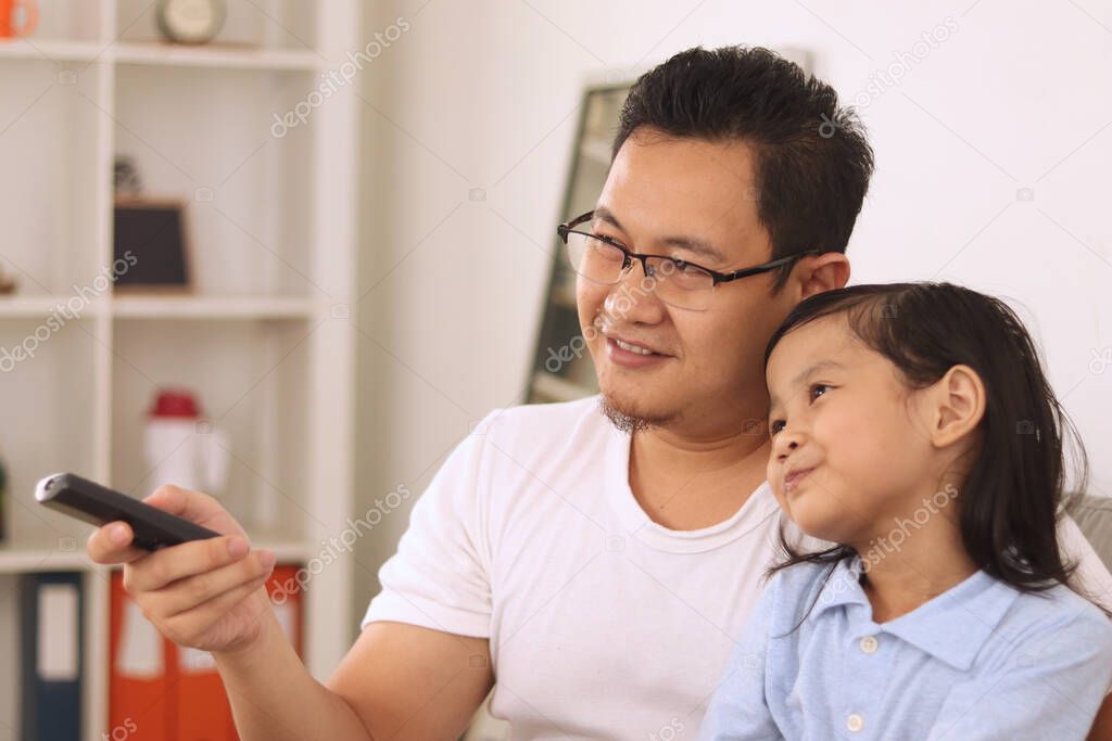 Asian father watching tv with his young baby girl daughter, happy single parent concept. Parenthood of a dad and his cute kid