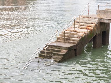 Dalgalı yeşil denize inen aşınmış beton merdivenler, metal parmaklıklarla yıpranmış beton merdivenler, sakin, yeşilimsi gri suya iniyor..