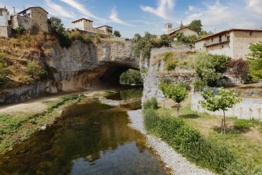 Durgun bir nehrin üzerindeki doğal kaya kemeri - Mavi gökyüzünün altındaki uçurumun tepesinde antik evler bulunan doğal bir kaya kemerinin içinden akan bir nehir..