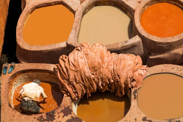 Fas 'lı bir tabakhanede, farklı renklerde tabakhanelerle çevrili geleneksel bir boya fıçısına batırılmış bir işçinin tepeden görünüşü..