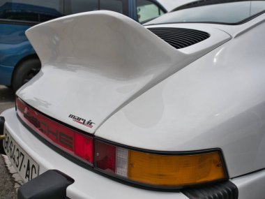 Klasik bir Porsche 'nin arka çeyreği - Beyaz bir Porsche 911' in arka görüntüsü, geniş spoiler, motor ızgarası, stop lambası ve bir marka çıkartması sergileniyor.