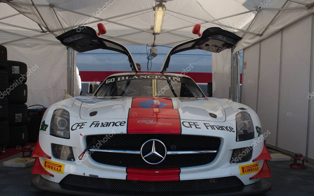 Mercedes-Benz Race Car with Gullwing Doors - A white Mercedes-Benz sports car with its iconic gullwing doors open, parked inside a team's pit garage, ready for a race.