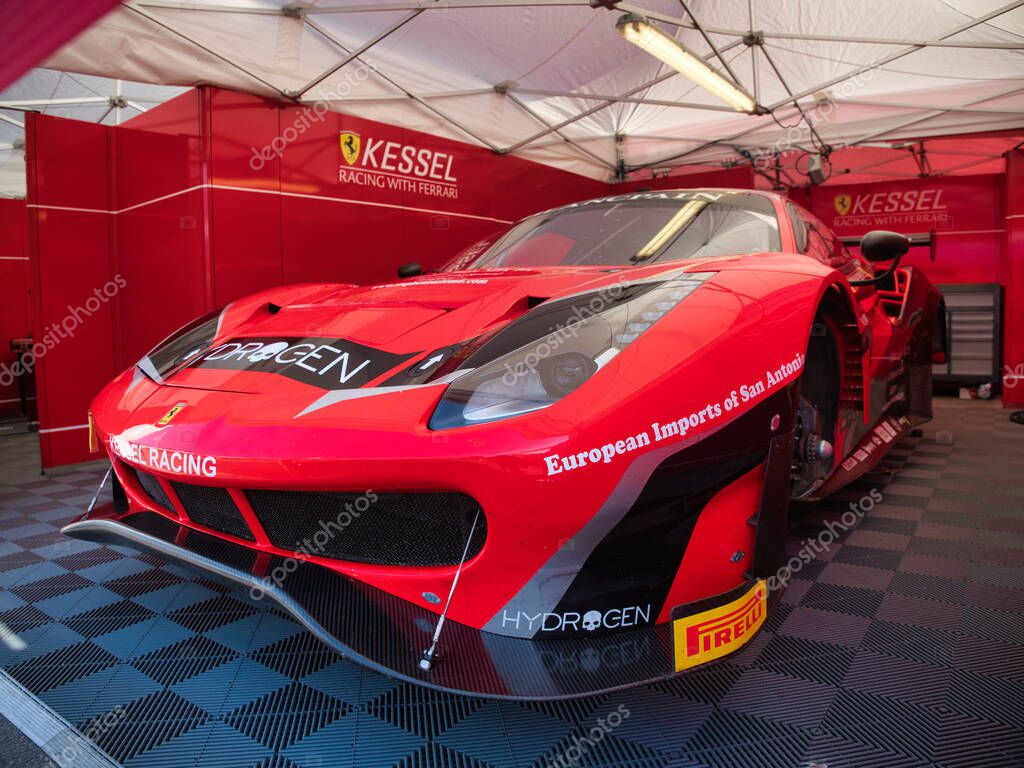 High-Performance Ferrari Race Car in Pit Garage - A detailed shot of a red Ferrari race car parked inside a professional pit garage, showcasing its aggressive design and team branding.