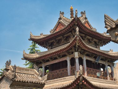 Çin Tapınağı 'nın süslü saçakları - geleneksel bir Çin tapınağının karmaşık, çok katmanlı saçaklarının yakın görüntüsü, detaylı, yıpranmış bir tasarım ve parlak mavi gökyüzü altında ince bir ışık ve gölge oyunu içerir..