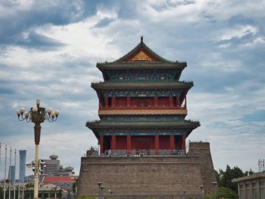 Geleneksel, çok katmanlı bir çatısı ve canlı kırmızı bir cephesi olan tarihi bir Çin kulesi dramatik, bulutlu bir gökyüzüne karşı duruyor, antik mimari ve kültürel mirası temsil ediyor..