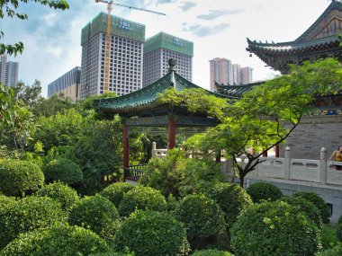 Eski Tapınak ve Yeni Gökdelenler - Yeşil kiremitli çatısı ve pagoda ile çevrili klasik bir Çin tapınağı, arka planda modern gökdelenlere ve inşaat vinçlerine karşı keskin bir görsel karşıtlık yaratır..