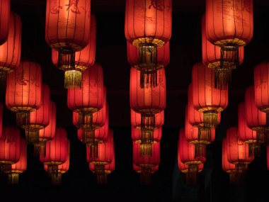 Parlak Kırmızı Çin Fenerleri - Altın püsküllü ve geleneksel yazıtlı bir grup parlak kırmızı Çin fenerinin yakın plan, karanlık bir arkaplana karşı düzgün sıralarda asılı, şenlik ve iyi şans simgesi.