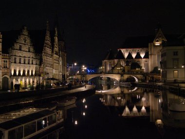 Ghent Kanalı ve Gece Kilisesi - Leie Nehri 'nin tarihi St. Michael Köprüsü ve aydınlık binalarla dolu gece manzarası.