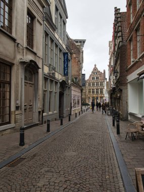 Tarihsel Gent 'teki Çakıl Taşı Geçidi - Gent' te dar bir kaldırım taşı sokağının kaldırım manzarası, geleneksel binalar ve uzak süslemelerle dolu.