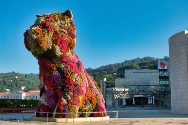 Bilbao 'daki Puppy ve Iberdrola Kulesi - Çağdaş Iberdrola Kulesi ve arka planında açık mavi gökyüzü olan çiçeksi köpek heykelinin geniş bir görüntüsü.