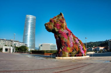 Bilbao 'daki Puppy ve Iberdrola Kulesi - Çağdaş Iberdrola Kulesi ve arka planında açık mavi gökyüzü olan çiçeksi köpek heykelinin geniş bir görüntüsü.