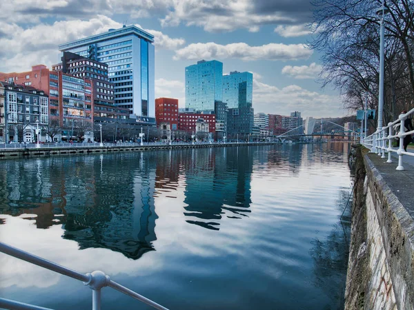 Bulutlu bir günde Bilbao şehir manzarası yansıması. Bilbao 'nun modern ufuk çizgisi, kuleleri ve binaları Nervin Nehri' nin sakin yüzeyine yansıyor bulutlu, dramatik bir gökyüzünün altında.