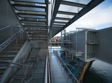 Modern Architecture Walkway Over Water - A metal and glass walkway with industrial design leads over water, reflecting the sky and clouds with a futuristic feel.