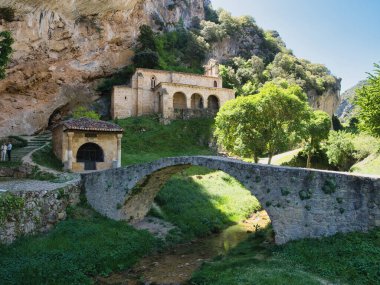 Köprüde Keçi olan Dağ Manastırı - Küçük bir nehrin üzerindeki taş bir köprüde duran kara keçi, arka planda sarp ve kayalık bir uçurumun kenarına inşa edilmiş tarihi bir manastır.