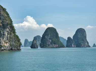 Striking Halong Bay limestone karsts - A scenic view of the massive limestone karsts rising majestically from the tranquil waters of Halong Bay, under a brilliant blue sky with clouds.