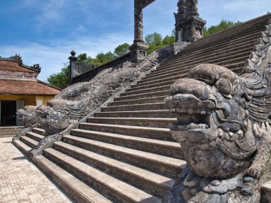 Tapınak merdivenlerini koruyan süslü taş ejderha heykeli, temiz bir gökyüzünün altındaki bir pagoda 'ya çıkan merdiven tırabzanındaki yıpranmış taş bir ejderhanın detaylı ve yakın çekim görüntüsü..