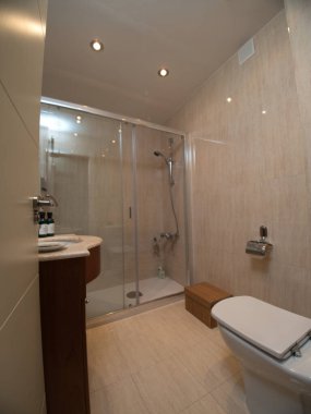 Cam duşlu geniş modern banyo, cam kapılarla çevrili büyük bir banyo, kıvrımlı lavabosu olan modern bir kibir ve bej kiremitli duvarlar..