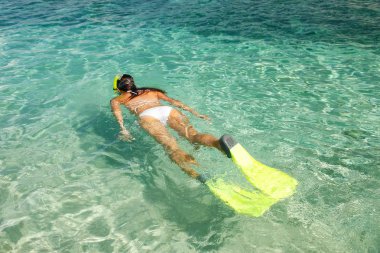 Genç bir kadın tropik adanın yakınlarındaki açık sığ sularda şnorkelle yüzüyor.
