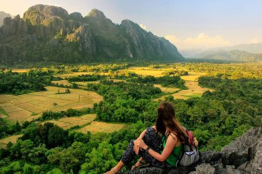 Young woman enjoying the view of farm fields in Vang Vieng, Laos. Vang Vieng is a popular destination for adventure tourism in a limestone karst landscape. clipart