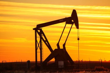 Gün batımında petrol sahasında siluetli pompa krikosu