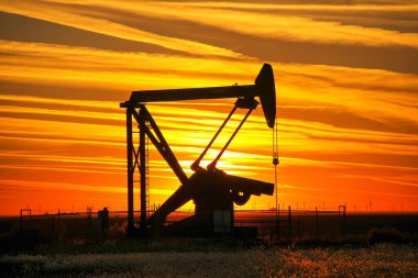 Gün batımında petrol sahasında siluetli pompa krikosu