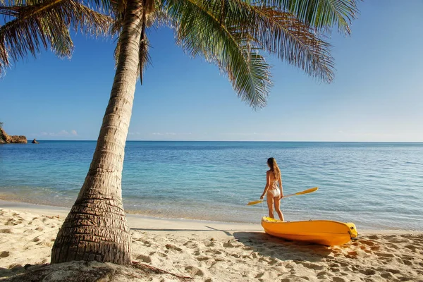 身穿比基尼的年轻女子站在沙滩上 有海上皮划艇和划桨 斐济纳库拉岛 — 图库照片