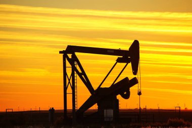 Gün batımında petrol sahasında siluetli pompa krikosu