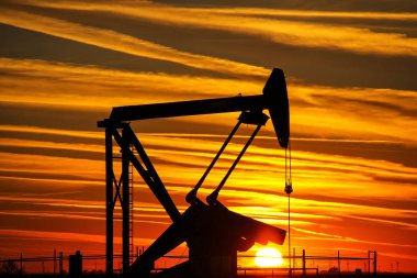 Gün batımında petrol sahasında siluetli pompa krikosu