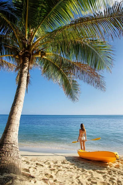 Ung kvinna i bikini stående på en sandstrand med havskajak en — Stockfoto