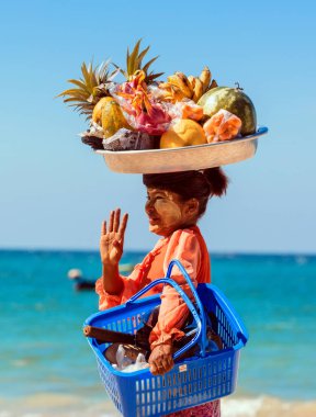 NGAPALI, MYANMAR - 5 HAZİRAN 2017: Kimliği belirsiz kadın turistlere taze meyve satıyor. Turistlere ürün satmak Ngapali plajındaki insanların ana geliridir..