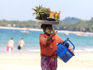 NGAPALI, MYANMAR - 5 HAZİRAN 2017: Kimliği belirsiz kadın turistlere taze meyve satıyor. Turistlere ürün satmak Ngapali plajındaki insanların ana geliridir..
