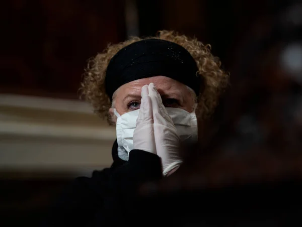 Senior woman in gloves and mask praying in a church