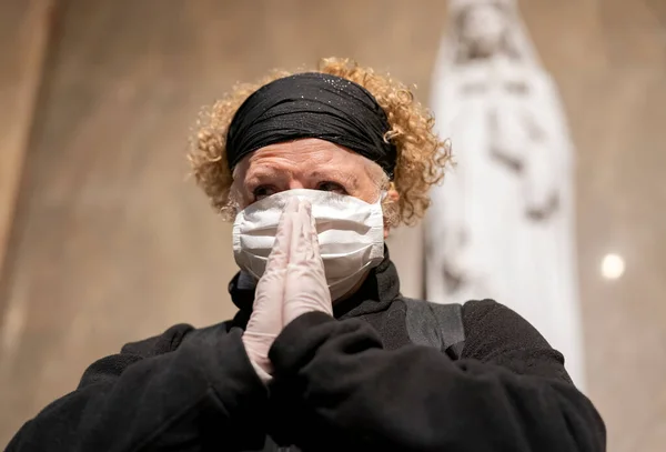 Senior woman in gloves and mask praying in a church