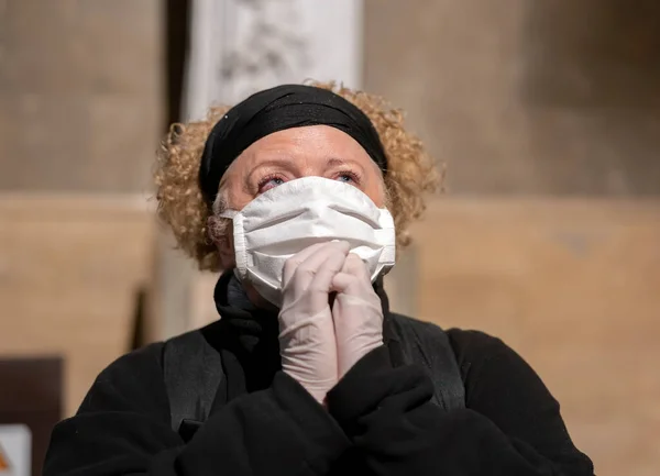 Senior woman in gloves and mask praying in a church