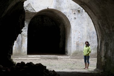 Yaşlı taş duvarda duran siyah elbiseli genç kadın.