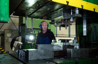 Fabrikada işçi, endüstriyel makinede çalışıyor.