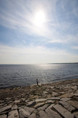 Bir adam sahilde duruyor ve ufka bakıyor.